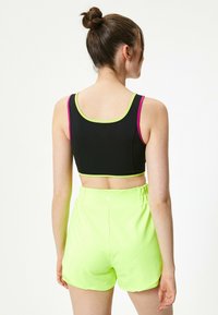 Sort sportsbh med neongrønne og pink accenter, parret med højtaljede neongrønne shorts. Glat, strækbart materiale; atletisk pasform.