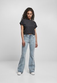 Svart kortärmad t-shirt med uppvikt ärm, kombinerad med ljusblå utsvängda jeans. Modellen har på sig vita skor. En enkel, avslappnad design.