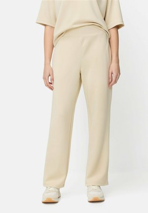 Beige vidde bukser i glat stof med elastisk taljebånd. Kombineret med en løs beige top og lyse sneakers.