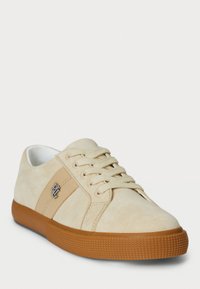 Beige suede sneakers with a textured gum sole, lace-up design, and a silver logo accent on the side. Smooth inner lining.