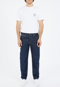 White cotton t-shirt with a small turquoise triangle logo on the chest, paired with dark blue denim jeans and white sneakers.