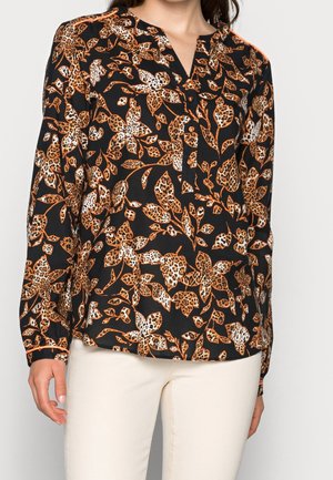 Sort bluse med lange ærmer med orange og hvid leopardblomstret print, knaplukning på kraven, båret med lyse beige bukser.