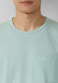 Mintgroene t-shirt met korte mouwen en een ronde hals, voorzien van een borstzak en een zachte, gestructureerde stof.