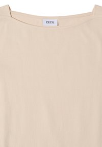 T-shirt beige à col rond avec une petite étiquette blanche cousue à l'intérieur du col portant la mention "CECIL" en lettres noires.