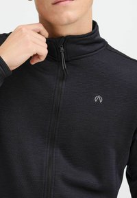 Giacca nera con zip realizzata in tessuto testurizzato, con colletto alto, caratterizzata da un logo discreto sul lato sinistro del petto e una zip a contrasto.