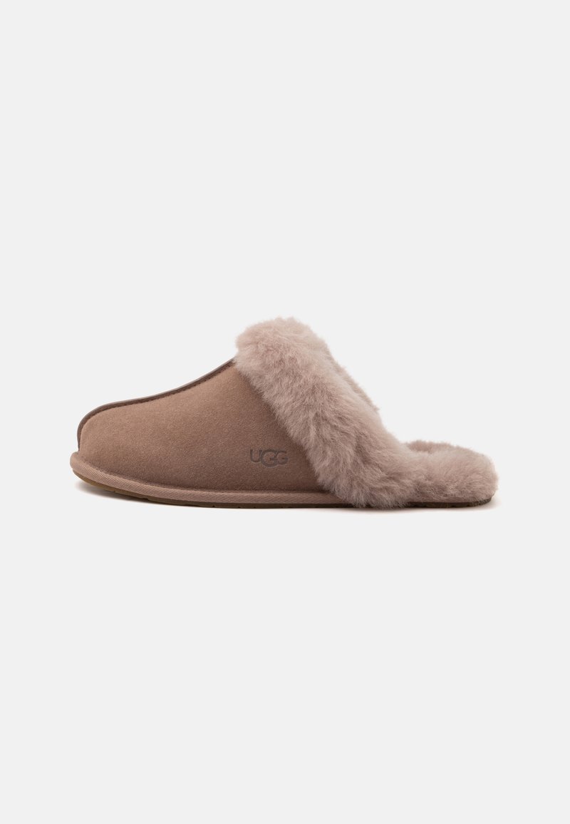 Καφέ παντόφλα τύπου slip-on με μαλακή, αφράτη επένδυση από γούνα και διακοσμητικά, με χαμηλό τακούνι και εξωτερικό υλικό που μοιάζει με σουέντ.