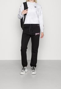 Šedá mikina s batikovým vzorem a logem, černé tepláky s růžovým nápisem "CHAMPION" a masivní bílé tenisky. Batoh nošený na jednom rameni.