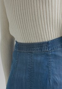 Ljusbeige ribbstickad tröja kombinerad med en blå jeanskjol med smockad midja och subtila sömmar, som visar upp en slät textur.