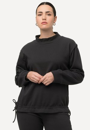 Felpa nera con colletto alto, texture a coste e orlo con coulisse. Presenta dettagli laterali con zip e maniche lunghe e ampie.