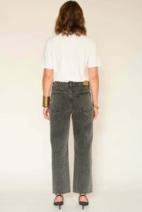 Jean noir taille haute à jambes larges avec une texture délavée, cinq poches et une étiquette sur la ceinture arrière. Le mannequin porte un t-shirt blanc.