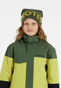 Veste à blocs de couleur verte et jaune avec une fermeture éclair à l'avant, un col haut et un logo. Le bonnet arbore le mot "PROTEST" en jaune.