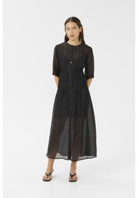 Black, semi-sheer long dress with a button-down front, 3/4 sleeves, gathered texture, and a straight silhouette, paired with black sandals.