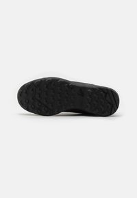 Schwarze Sneaker-Sohle mit strukturierter GummOberfläche. Verfügt über multidirektionale Stollen für Grip und ein Logo-Detail in der Nähe der Ferse.