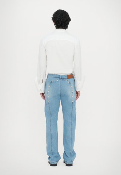 Világoskék farmernadrág magas derékkal, egyenes szárú, ezüst patent gombokkal a külső varrások mentén. Fehér, hosszú ujjú pólóval párosítva.