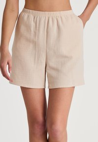 Beige, lichte shorts met een elastische tailleband en zijzakken. Heeft een subtiele textuur met een rechte snit tot halverwege de dij.