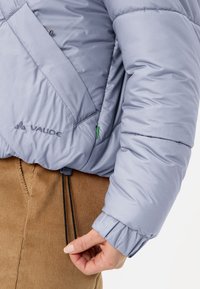 Giacca a vento azzurro chiaro con tessuto strutturato, dotata di cerniera parziale, tasche laterali e coulisse regolabile all'orlo.