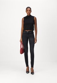 Top corto negro sin mangas, jeans ajustados oscuros, tacones altos negros, sosteniendo un bolso rojo, con una textura suave y un diseño minimalista.