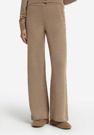 Pantalons larges en tricot beige avec une taille côtelée et des détails de tricot en câble sur les côtés. Texture douce avec une coupe décontractée.