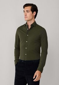 Camisa de manga larga verde oliva con diseño de botones, que presenta una textura suave y un detalle de interior del cuello en contraste. Corte ajustado y estilo de cuello clásico.