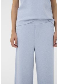 Hellgraue Hosen mit weitem Bein aus weichem, strukturiertem Stoff, ausgestattet mit einem flachen Vorderteil und Seitentaschen, kombiniert mit einem leicht locker sitzenden Oberteil.