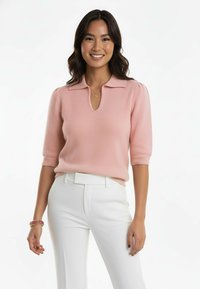 Jasnoróżowy sweter dzianinowy z małym kołnierzykiem, krótkimi rękawami i dekoltem z wycięciem typu keyhole, w zestawieniu z białymi spodniami i bransoletką z koralików.