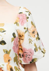 Λευκό φόρεμα με ροζ και πορτοκαλί λουλουδάτο μοτίβο, με φουσκωτά κοντά μανίκια και τετράγωνη λαιμόκοψη.