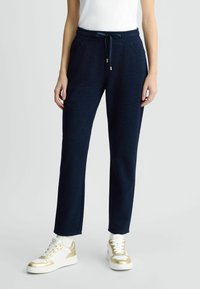 Jogging en bleu marine avec une texture mate, ceinture élastique et poches latérales. Doté d'un cordon de serrage avec des accents en métal doré.