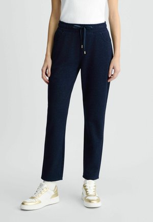 Jogging en bleu marine avec une texture mate, ceinture élastique et poches latérales. Doté d'un cordon de serrage avec des accents en métal doré.