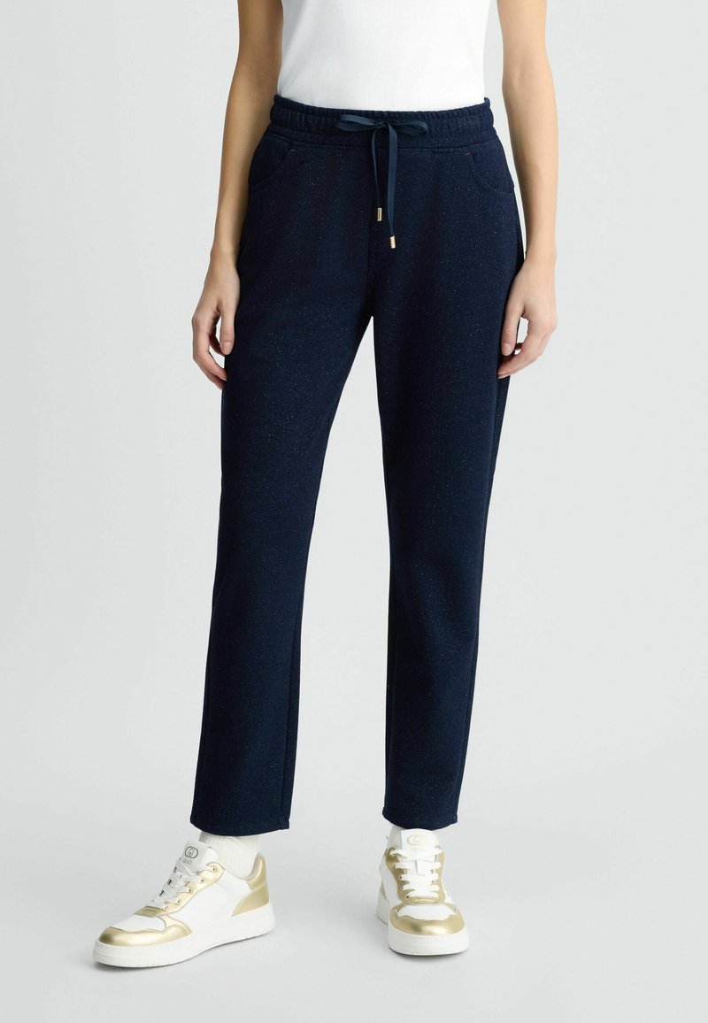 Jogging en bleu marine avec une texture mate, ceinture élastique et poches latérales. Doté d'un cordon de serrage avec des accents en métal doré.