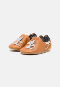 Leder Babyschuhe in Orange, mit einem weißen Einhorn-Design auf der Vorderseite, elastischem schwarzen Kragen und beigefarbenen Sohlen mit gestreiften Akzenten.
