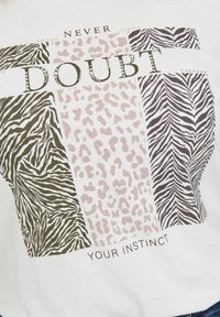 Biała koszulka z grafiką "Nigdy nie wątp w swoje instynkty". Wzory obejmują paski zebry w brązie i czerni oraz plamy lamparta w różu.