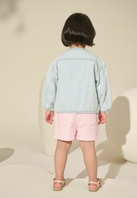 Hellblau gestreifte Jacke mit puffärmeln, kombiniert mit pinken Shorts, die einen strukturierten Stoff und zwei Gesäßtaschen aufweisen.