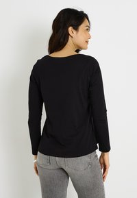 Camiseta negra de manga larga con escote redondo, textura suave y ajuste relajado, combinada con pantalones grises con textura.