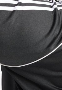 Černá látka s hladkou texturou má bílé vodorovné pruhy a kontrastní bílý detail podél zakřiveného lemu.