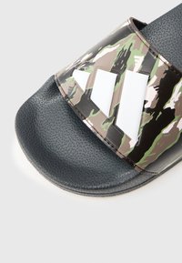 Kamuflasje-slip-in sandal med en glanset syntetisk overdel med grønne, svarte og brune mønstre; teksturert mørk såle for grep.