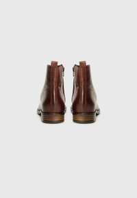 Bottines en cuir marron avec une finition lisse, fermetures éclair à l'arrière et un talon empilé. Elles possèdent un bout rond et des détails de couture subtils.