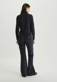 Haut à manches longues bleu marine avec col montant associé à un pantalon en velours côtelé évasé. Texture lisse, détails de couture subtils et accent de bouton en métal.