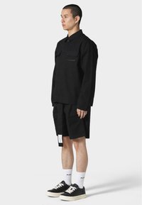 Black long-sleeve shirt with two chest pockets, paired with black cargo shorts. Worn with black sneakers and white ankle socks.