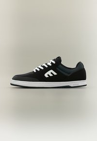 Μαύρο χαμηλό αθλητικό παπούτσι με λευκά κορδόνια, λευκό λογότυπο "E" στο πλάι και λευκή λαστιχένια σόλα, παρουσιάζεται σε ουδέτερο φόντο.