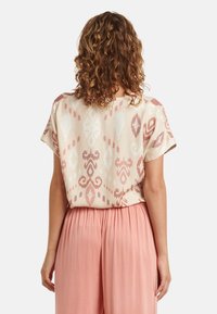 Short-sleeve blouse in light beige with pink and white ikat patterns. Soft fabric with a relaxed fit, paired with peach pleated pants.