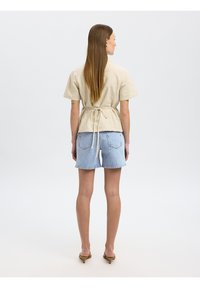 Haut à rayures beige à manches courtes avec un lien ajustable à la taille, associé à un short en denim clair. Texture lisse, coupe décontractée, design minimaliste.