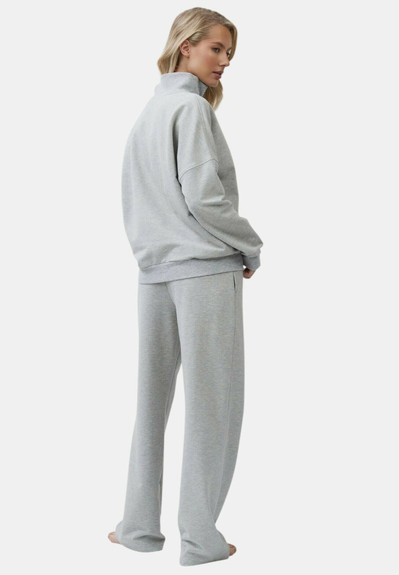 Felpa grigia chiara con colletto alto, vestibilità rilassata e pantaloni della tuta coordinati a vestibilità ampia. Materiale morbidamente misto cotone, dettagli minimi.