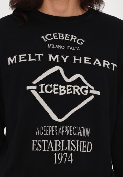 Pull en tricot noir avec un texte blanc incluant "ICEBERG," "MELT MY HEART," et un graphique en forme de cœur. Encolure ronde côtelée, coupe décontractée.