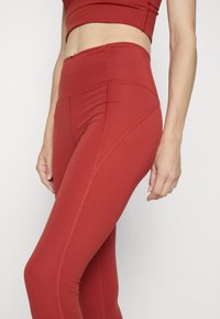 Leggings rojos de cintura alta, hechos de un material elástico con una textura suave; cuenta con costuras y un diseño ajustado.