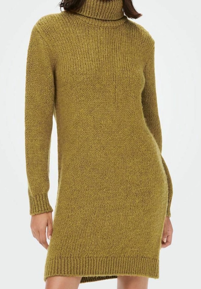 Femme portant une robe-pull à col roulé tricotée vert olive à manches longues, debout devant un fond uni.