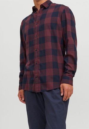 Camisa de botones en un patrón de cuadros en rojo oscuro y azul marino, de mangas largas, con cuello y botones negros. Tela suave con textura visible.