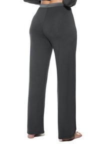 Persoon blootsvoets in donkergrauwe high-waisted, wijde broek, gezien van achteren met de armen gekruist boven de taille.