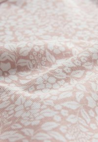 Svetloružová tkanina s bielymi kvetinovými vzormi, s ryhovanou textúrou. Dizajn obsahuje listy a kvety v jemnom, opakujúcom sa motíve.