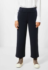 Navy wide-leg pants with a flat waistband. Soft material, paired with a white long-sleeve shirt and brown high-top sneakers.