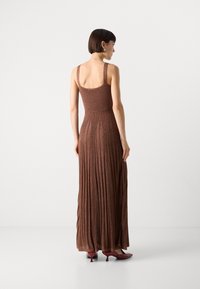 Maxikleid aus braunem Textilgewebe mit tailliertem Oberteil und plissiertem Rock. Verfügt über breite Träger und wird mit burgunderfarbenen High Heels kombiniert.